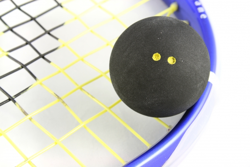 Squashbal met twee gele stippen op de besnaring van een squashracket