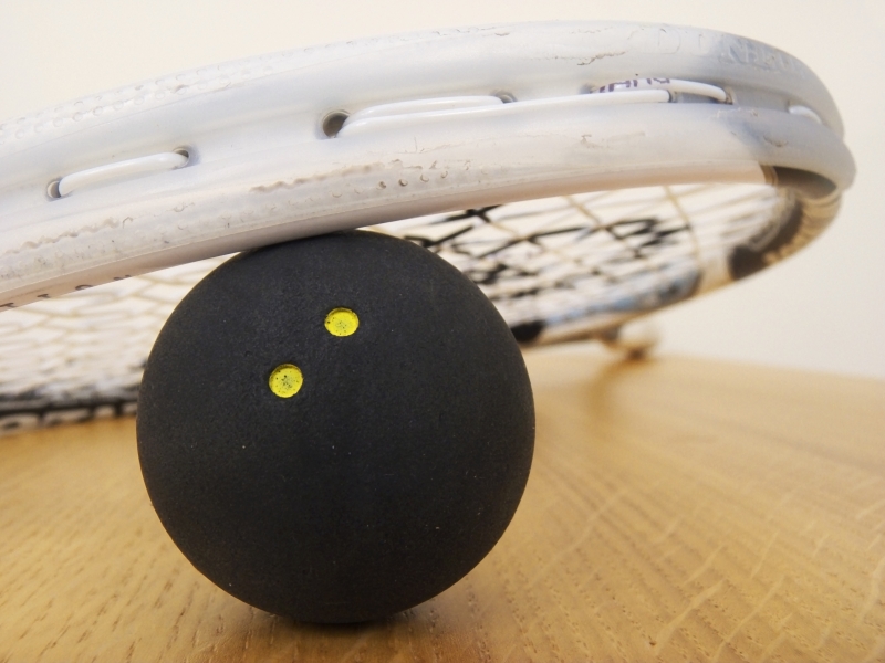 Zwarte squashbal met twee gele stippen naast een squashracket